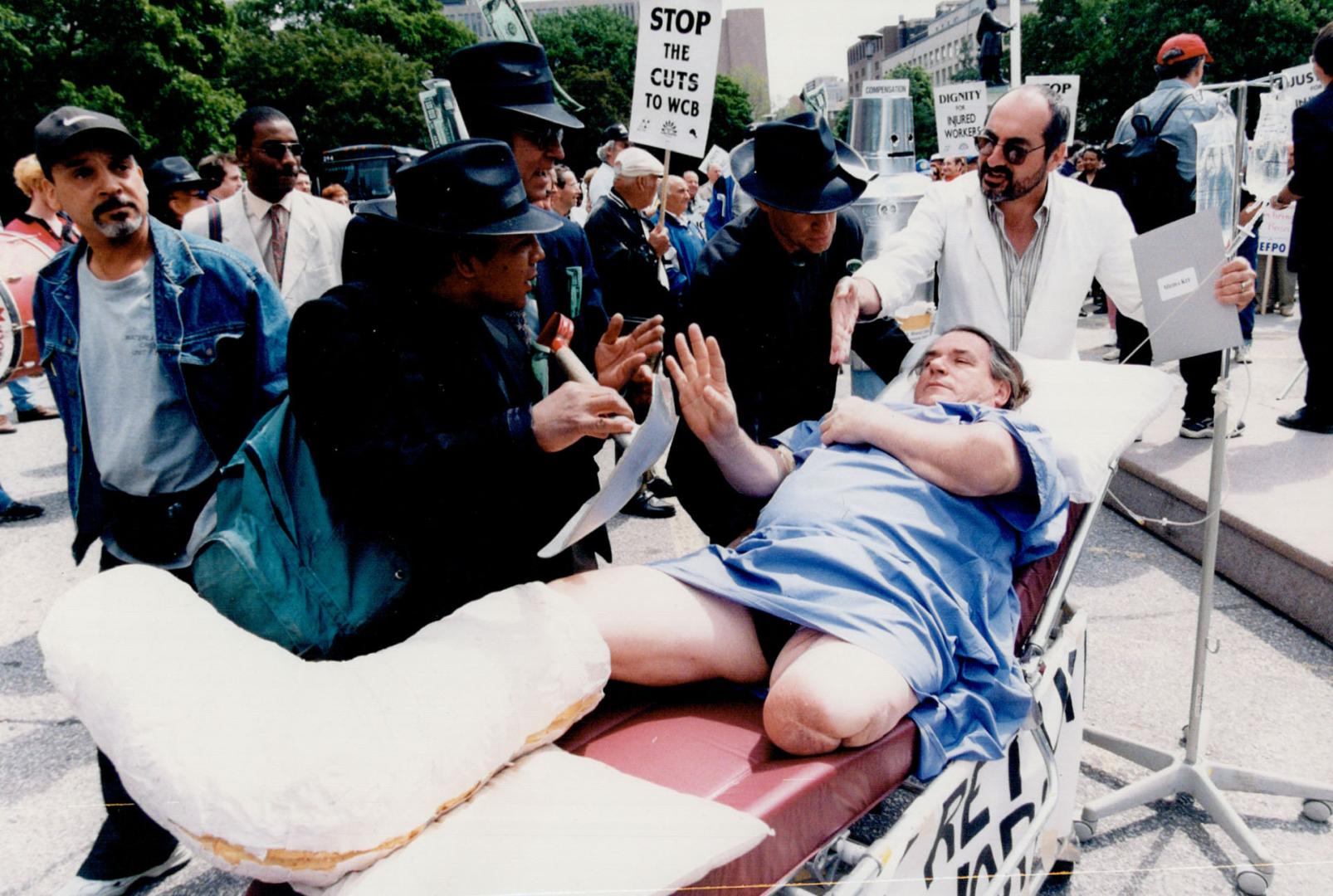 Queen's Park Rally: Richard Hudon, 54, who lost a leg in a work accident at 17, pretends to be an injured worker being ordered back to work by business types