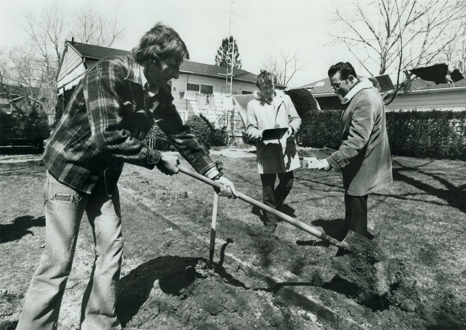 Mr. Stuart Pearson is working in his backyard while Stuart Morley and Bruce Thomson (in raincoat) are taking Geiger counter readings