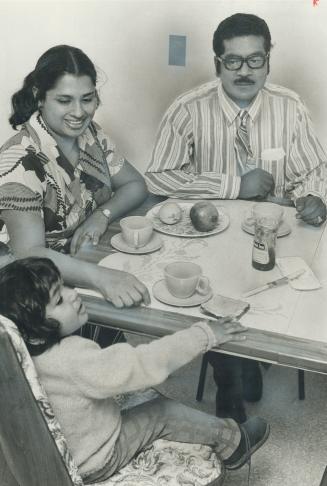 Youngest new arrival from Uganda, Clement de Souza, 3, sits at table with father and mother, Mr