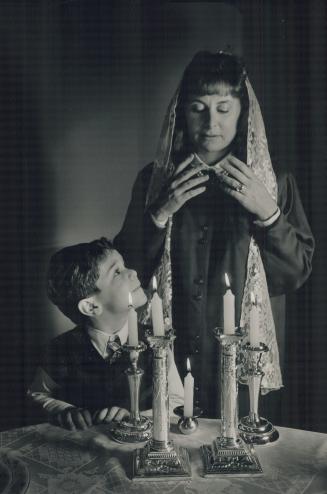 Lighting candles to honor the arrival of the Sabbath on a Friday night, Sarah Zinman prays with the traditional gestures as son David looks on. The nu(...)