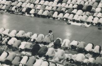 Overhead view of large number of people bent over praying with a young girl standing and a path…