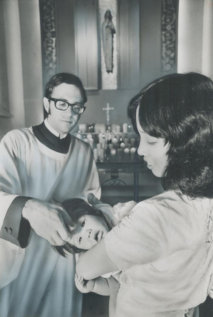 Baby Marizza Christine, daughter of Aniceto and Theresita Obtinario, is held by her mother while she is baptized by Rev