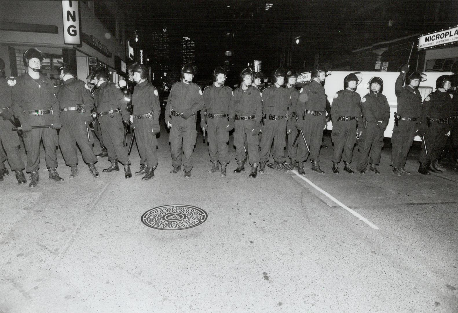 A wall of police officers block off a street as looters, inset, plunder a store in Toronto in May