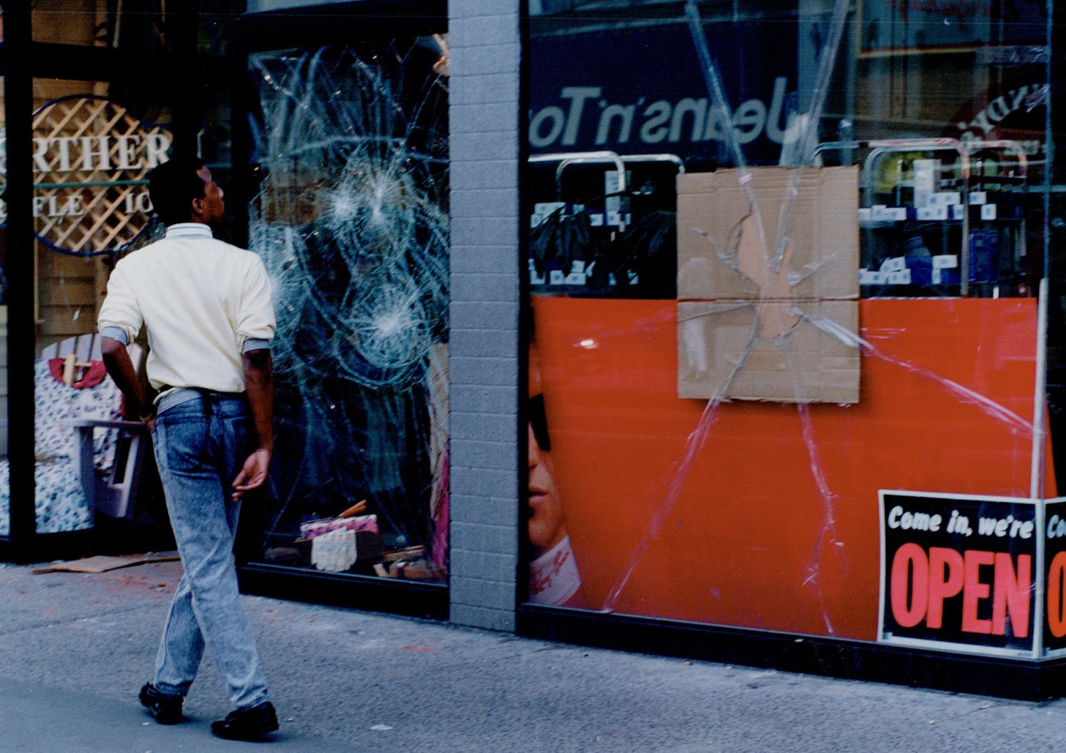 A pedestrian passes shattered windows on Yonge St