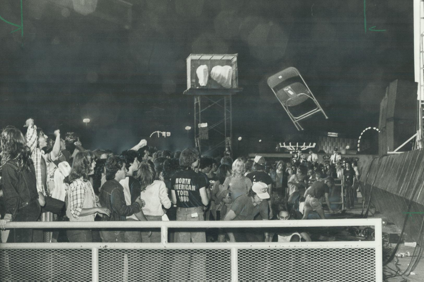 Rock fans close to the Grandstand stage cheer as chair flies through the air during rioting last night after Alice Cooper show was cancelled