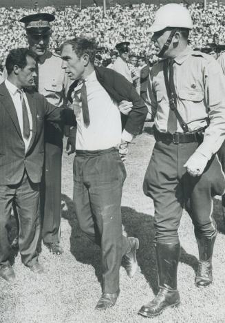 Off he goes: The battle over, the policeman escorts the subdued fan from the Varsity Stadium field