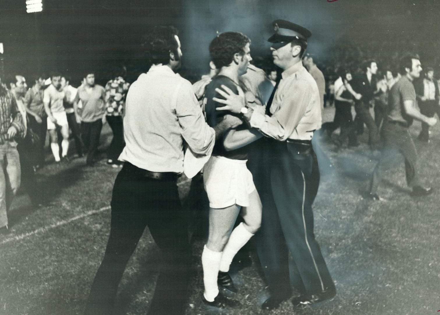 Police constable restrains a Dinamo Zagreb player during last night's wild brawl which forced cancellation of exhibition soccer game with Greek team at the CNE