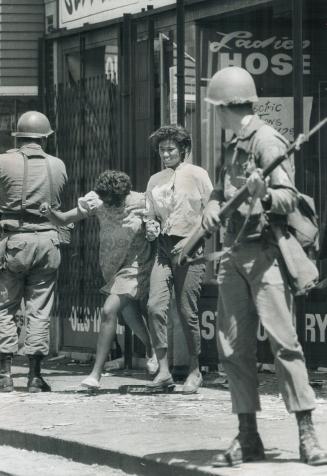 Fleeing the scene: Two Negro girls run from a Detroit shop as a national guardsman, bayoneted rifle at the ready, one of 8,000 in the embattled city, looks on