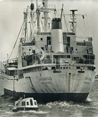 It's business before pleasure, A tiny boat rides perilously close to the stern of the cargo ship Cap Castillo as it passes through the break-water and(...)