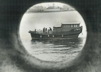 A Chinese junk from Hong Kong rides at anchor in Toronto harbor, seen through a porthole of another ship