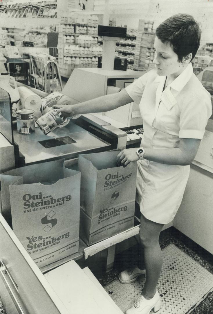 Montreal supermarket cashier Lynne Bourgie passes food items over glass which reads pricing code on each article