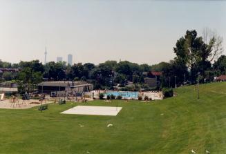 Image shows a playground and a pool with some trees in the background.