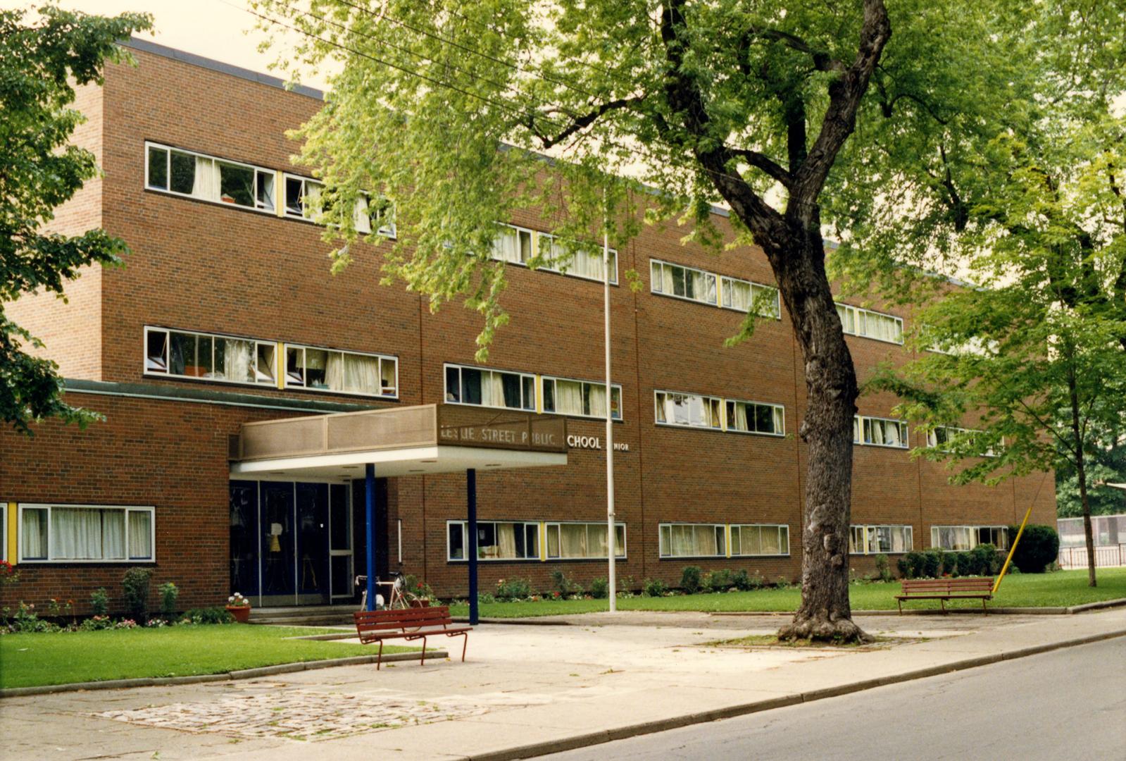 Image shows a three storey school building from the street side with some trees in front of it.