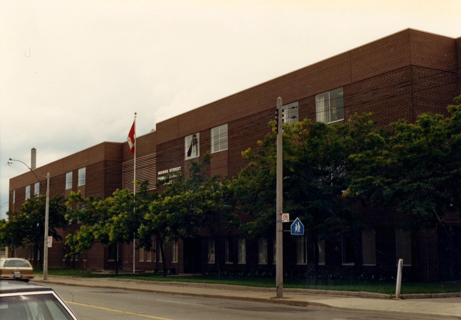 Image shows a three storey school building from the street side with a number of trees in front…