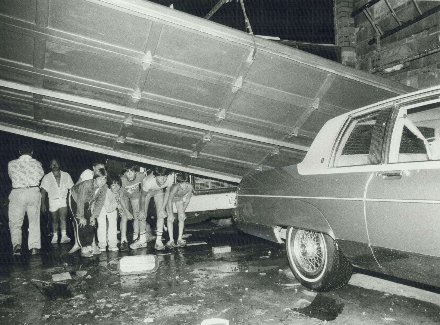 Tony Pennacchio, whose roof was blown across the road, checks the damage, while kids take a peek into his garage