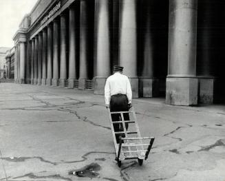 Last redcap. Dragging his empty handcart behind him this lonely redcap heads across the deserted approach to the main entrance at Toronto's Union Stat(...)