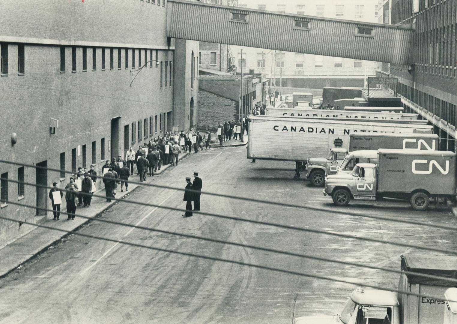 Members of the striking Teamsters Union parade along narrow sidewalk on Station St