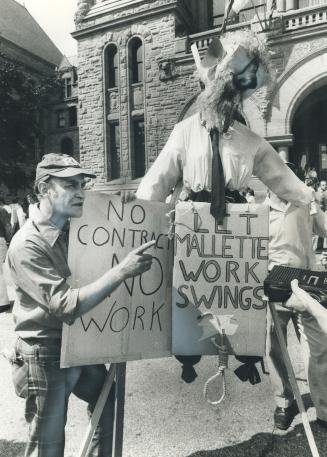 Protesting legislation ordering him back to work, this TTC man shakes his finger angrily in front of legislature yesterday. Next to him is a dummy of (...)