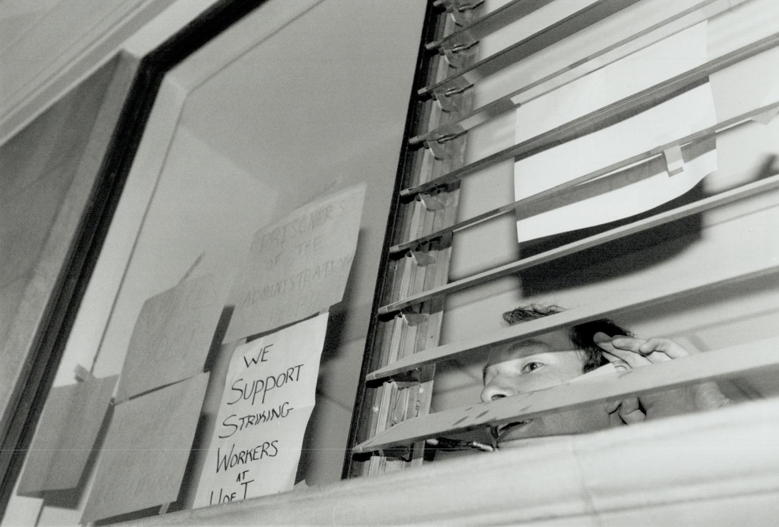 Striking view: One of the University of Toronto students who yesterday occupied the president's office peeks out a window after messages were posted supporting striking staff