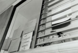 Striking view: One of the University of Toronto students who yesterday occupied the president's office peeks out a window after messages were posted supporting striking staff