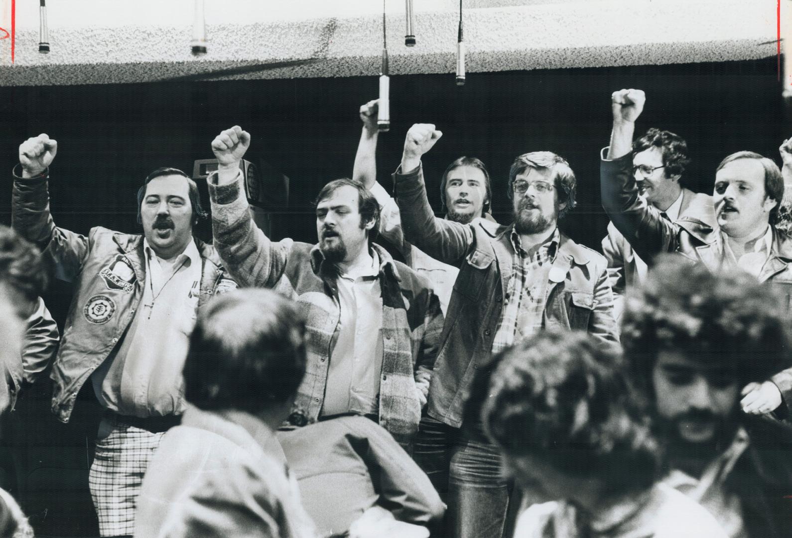 Inside postal workers in Ottawa raise their arms in a salute to union solidarity