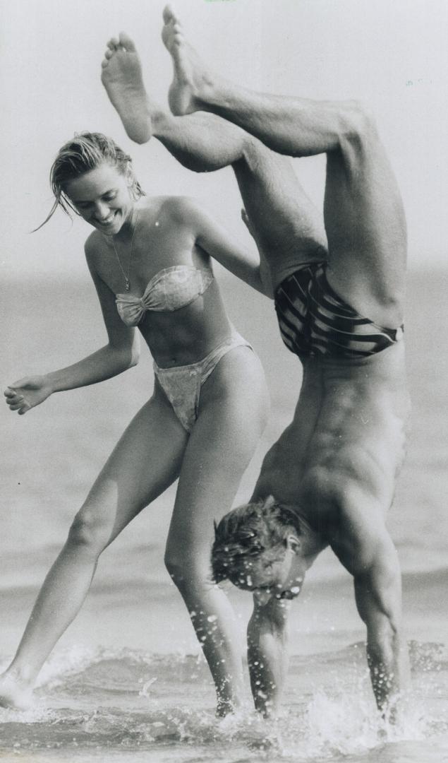 Head over heels, Bogden Sobilo of Toronto does his best to impress Karen Minda yesterday at Woodbine Beach by walking on water with his hands. Forecas(...)