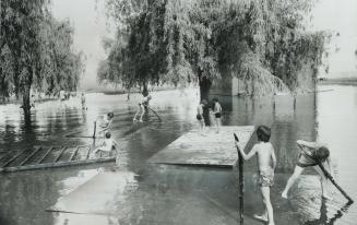 Come on in -- the water's fine, Boys use sections of the Coronation Park bandshell as rafts yesterday in a flooded section of the Oakville park, inun(...)