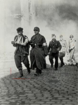 A group of German prisoners, including a wounded man, left, leave the flaming city under guard of a U