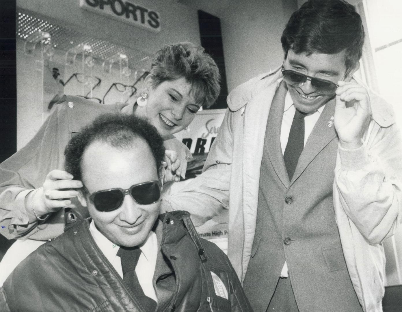 Helping hand for blind visitor, Lucio Rosales, left, and Mario Tulio Lopez, members of a choir of blind students from Honduras visiting Metro, try on sunglasses at Imperial Optical Canada