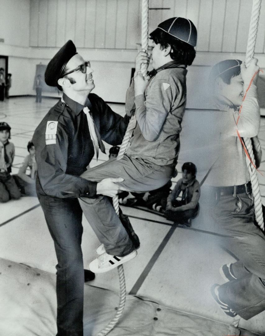 Father Salvatore Denaro helps cub climb rope in gym, Father Denaro is leader of newly organized 149th Cub Pack