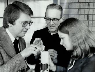 John and Mary Huff are seen with Father Patrick German and are lighting a candle, a symbol of marriage encounter program priest conducts. The Huffs, w(...)