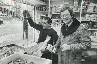 Rev. Joao Carlos Keidann, right, talks to parishioner Amador Fernandez in Fernandez' fish store on Dundas St. W