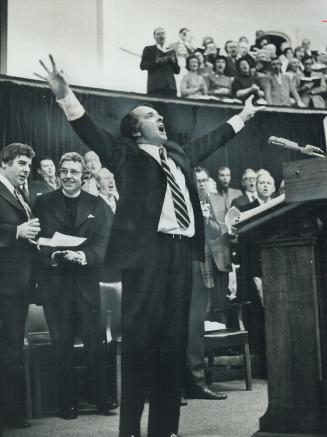 Leading 1,400 persons in singing old familiar hymns, Rev. Hedd-Wynn Williams conducts a hymnfest last night in Convocation Hall at the University of Toronto