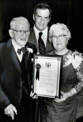 Clarence, 86, and Aida Purcell, 84, accept plaque from MPP William Newman at party