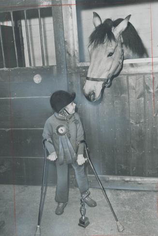 Prizewinner talks to her friend, Wearing her first-place ribbon and balancing on her crutches beside Junior Class riding trophy she won at first horse(...)