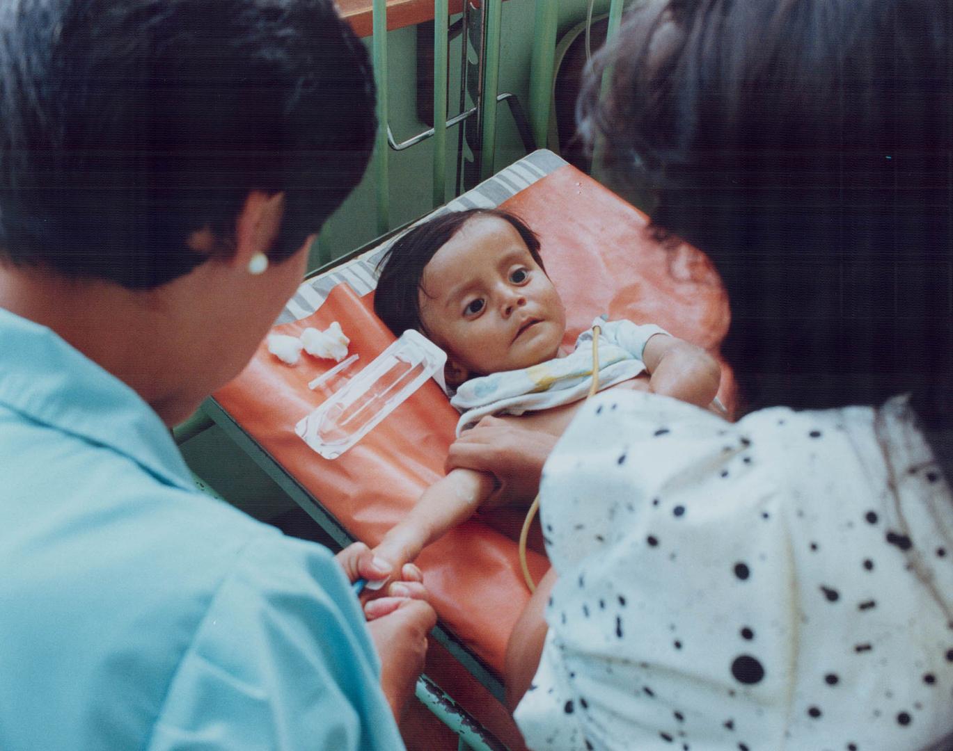 Cholera Peru - Young baby at Hospital De Apoyo Maria Auxiliadora suffering from cholera looking up at nurse and her mother