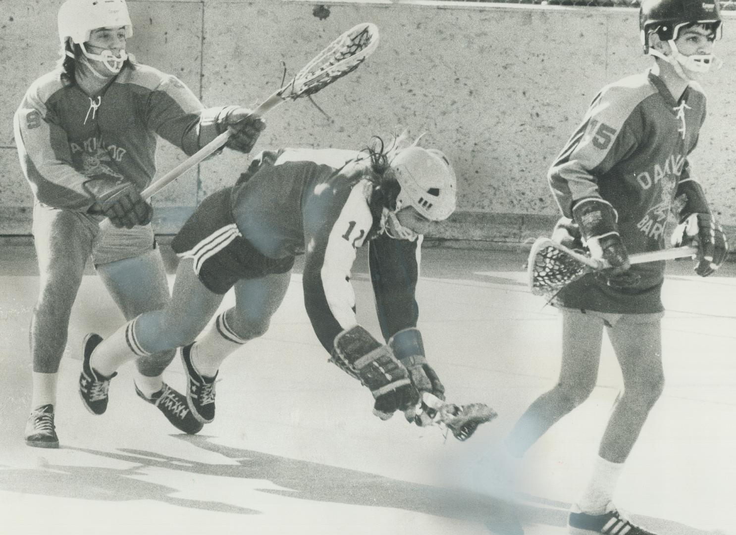 It's not cricket, but it's certainly typical of lacrosse as Oakwood Barons' Vic Badinetti (left) sends Gerry Mainville of Danforth Tech Redmen sprawli(...)