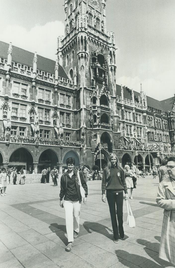 Fencer Donna Hennyey and high jumper Louise Hanna, both of Toronto, stroll in front of the Olympic city's famous old town hall