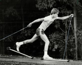 Young man using roller skis on a path through woods.