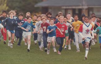 More than 30 young boys racing in a pack over grass.