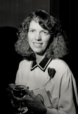 A young woman with curly hair, wearing a rose on her lapel, holds a glass of red wine and smile…