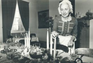 Pioneer Christmas, Evelyn Baker lights candles over the Christmas table in Halfway House at Pioneer Village at Steeles Ave. and Jane St. Decorations are going up all over the village