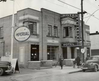 Two-story light brick building with sign overhanging sidewalk above entrance reading, Hotel Sag…