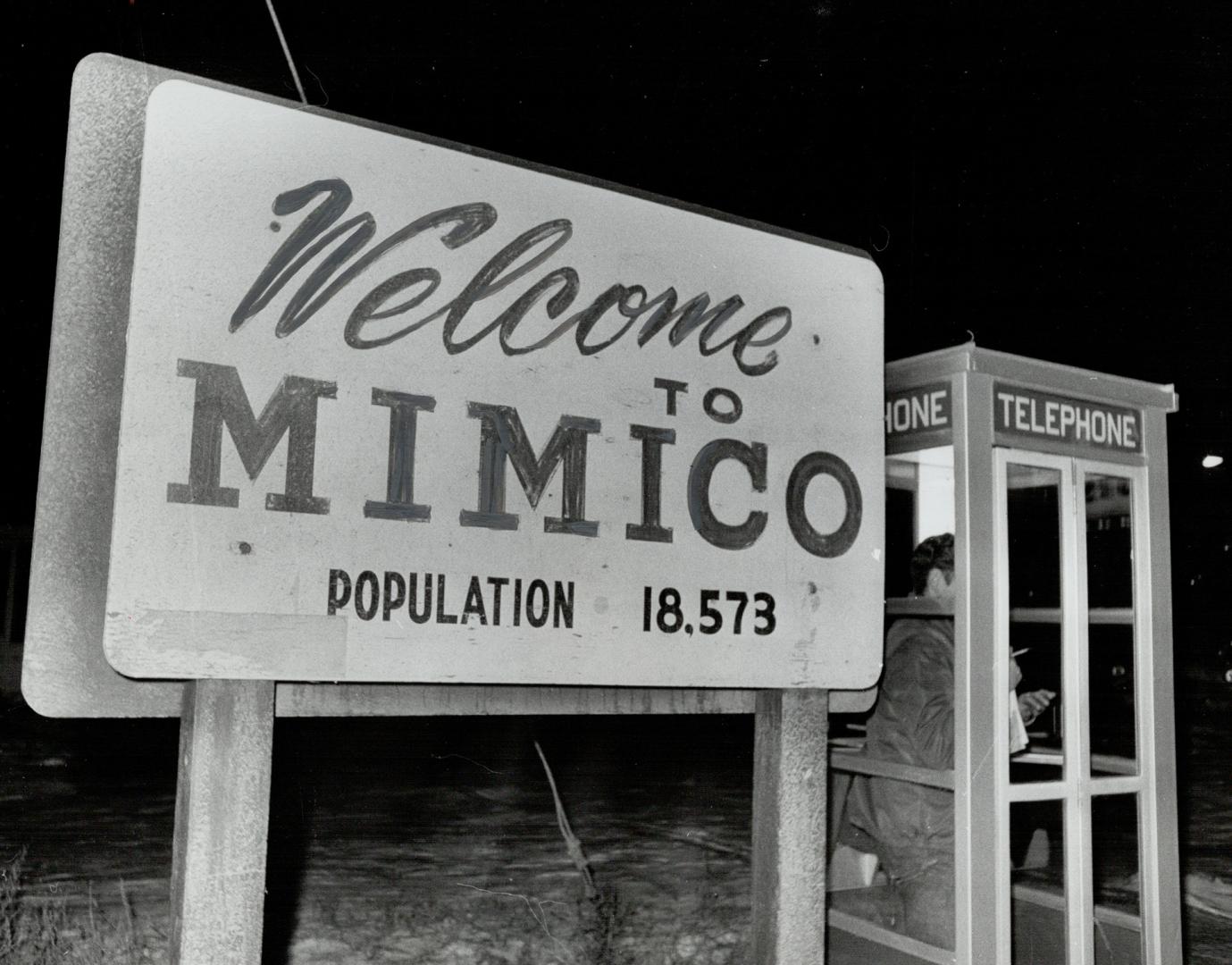 White sign affixed to two wooden posts displays the text, Welcome to Mimico - population 18,573…