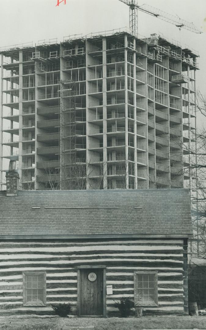 The old and the new. A 150-year-old log cabine owned by the Sentinel Rover crew of Port Credit contrasts with apartment building being built. Cabin was moved from Peterborough