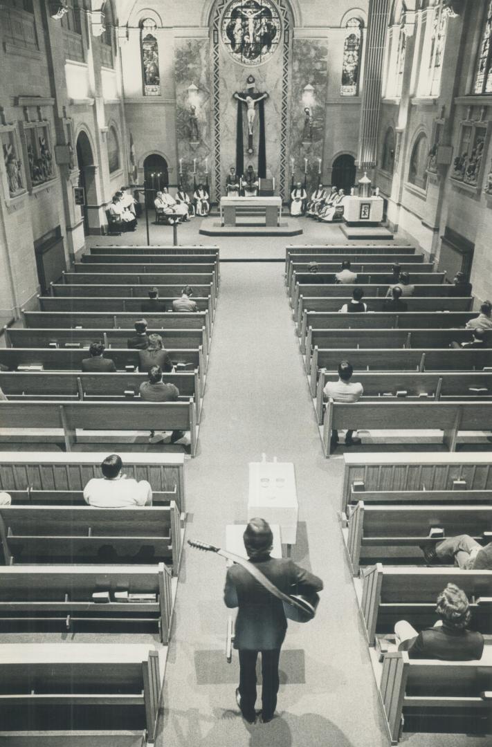 Overhead view of man with guitar standing in chapel aisle facing pulpit between two rows of spa…