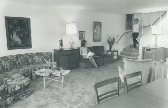 Living room of split-level apartment has staircase rising to bedroom level at the right