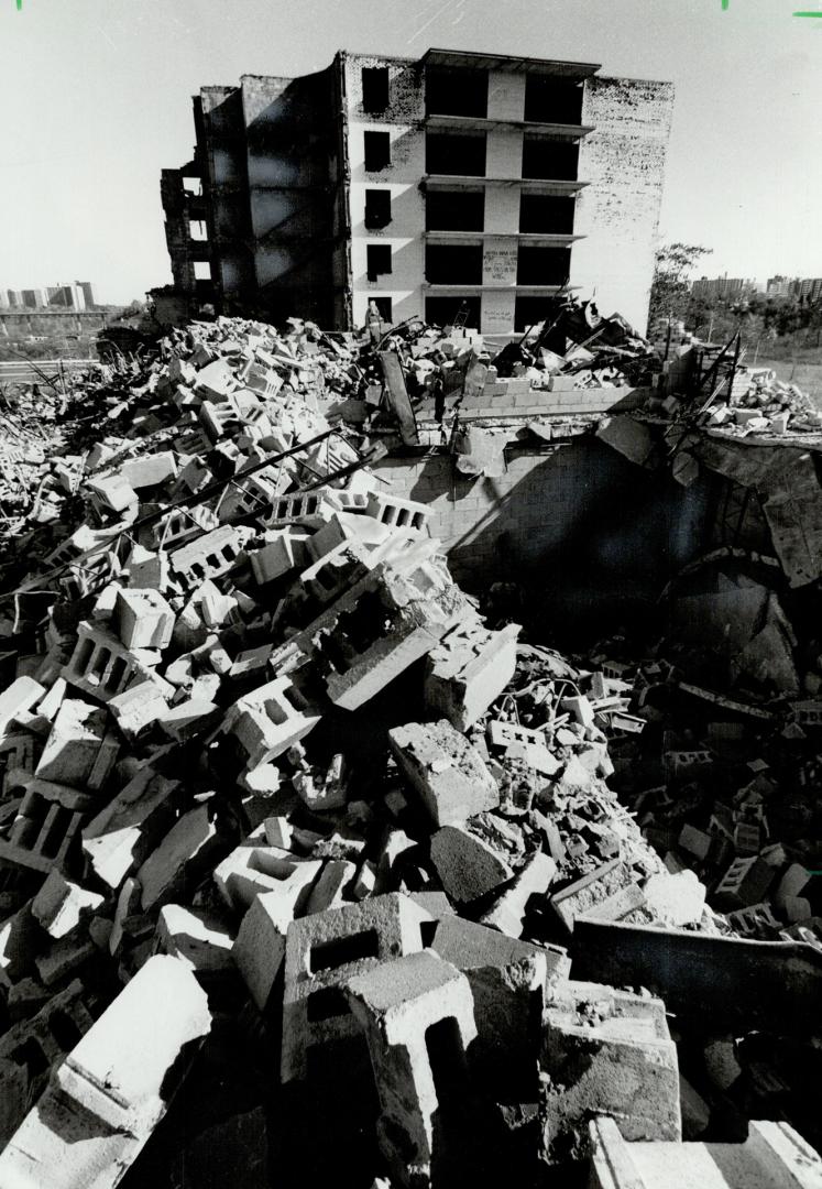 In the foreground, cement blocks and steel rods form a pile of construction rubble. Beyond the …