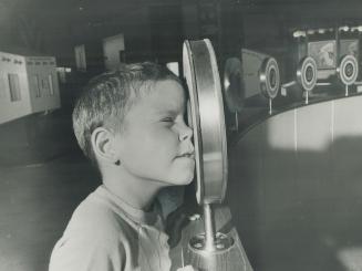 Optics. Another visitor, Garry Derry, peers through an eyepiece which creates an optical illusion that a wooden bar is actually passing through anothe(...)