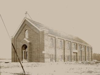 Exterior view of brick church with upper row of small arched windows along side, and cross affi…